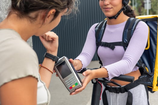 Unrecognized customer paying with smartwatch at card reader offered by delivery woman with backpack photo