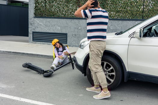 Driver holding head in distress after hitting Latin food courier with backpack and electric scooter photo