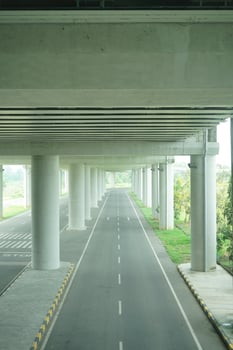 A long, straight road passing through a concrete overpass structure with multiple arched openings, surrounded by green foliage at new yogyakarta international airport photo