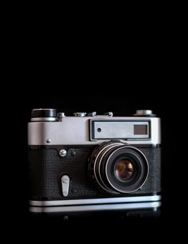 Vintage film camera on a black background, classic design, silver and black body, lens with aperture markings, textured grip. photo