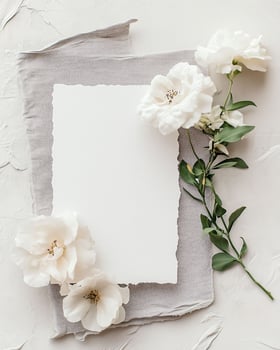 Creative flat lay composition with delicate white flowers arranged around blank card on white background, invitation photo