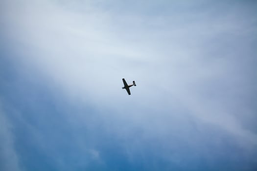 A small airplane flying against a backdrop of a clear blue sky with wispy clouds, creating a serene and open atmosphere photo