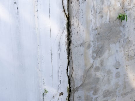 Grey cement walls of the house have dark cracks. Cracked concrete wall background photo