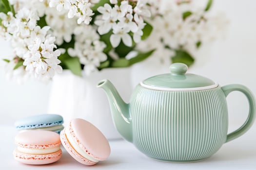 Refreshing herbal tea served in a muted green teapot with delicate macarons in pale pink and soft blue beside a bouquet of white flowers photo