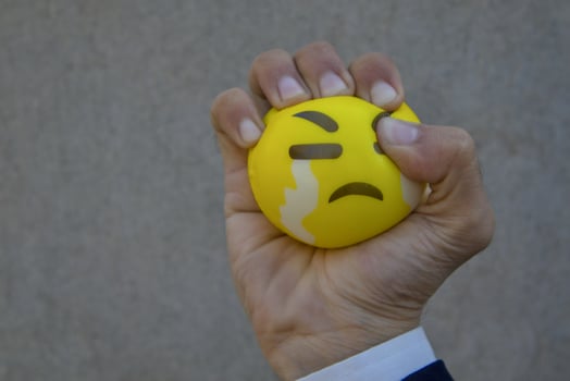 Hand Squeezing a Yellow Stress Ball with Crying Emoji photo
