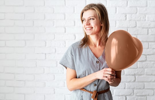 Mocha Mousse - color of the year 2025. Young woman holding heart shaped balloon on white brick wall background photo