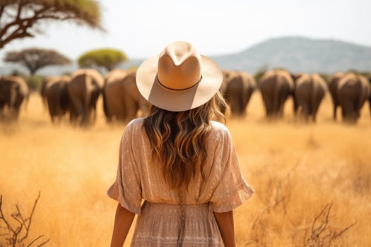 woman in hat standing in field of elephants photo