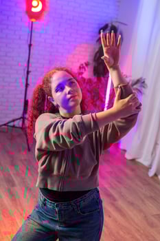 A young woman with red hair dances in a studio lit by pink and purple lights photo