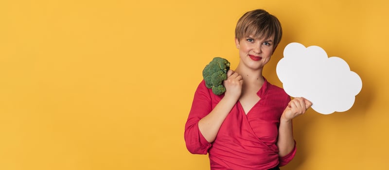 A studio shot of a young smiling woman holding fresh broccoli and a blank letterhead. The concept of healthy eating. photo