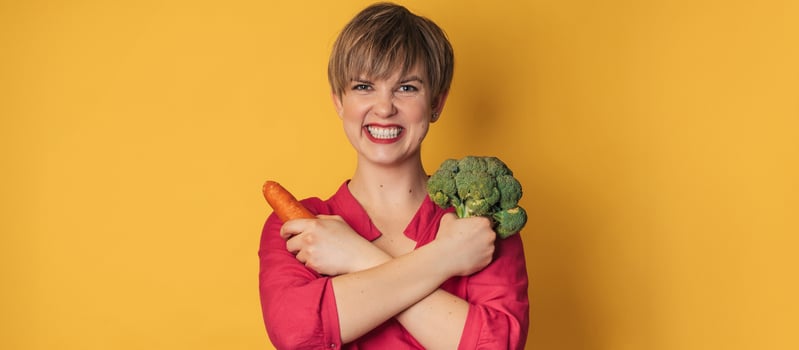 A studio shot of a smiling young woman with fresh broccoli and carrots in her hands on a yellow background. close-up.. The concept of healthy eating. A place for your text. The panorama. photo