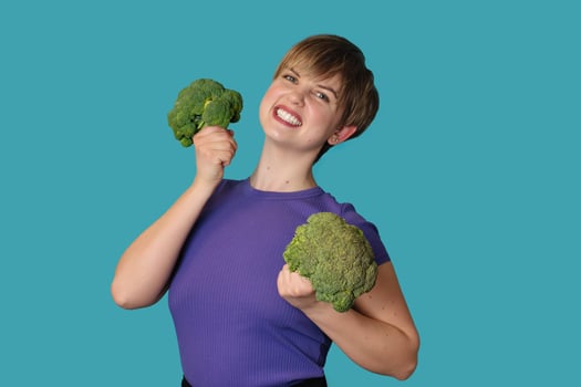 Broccoli in the hand of a slender smiling woman on a blue background. healthy lifestyle. photo