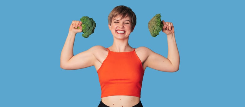 A smiling Caucasian girl with fresh broccoli in her hands as dumbbells. Panoramic banner, free space. photo