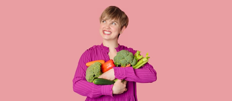 Studio shot, a young Caucasian woman holding a lot of fresh vegetables in her hands. The concept of healthy eating. Vegetarianism. photo