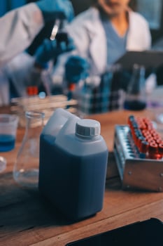 Two people in lab coats working on a table with a container of liquid photo