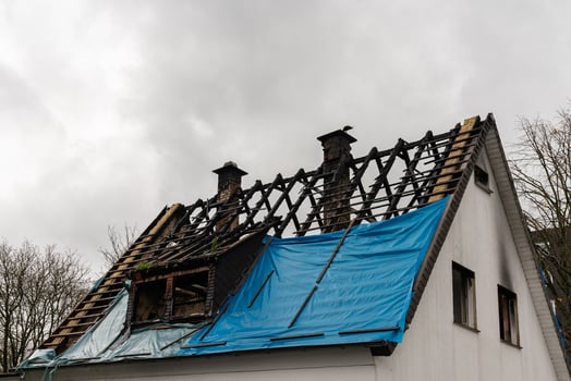 Fire damage visible on residential roof covered with blue tarp. photo