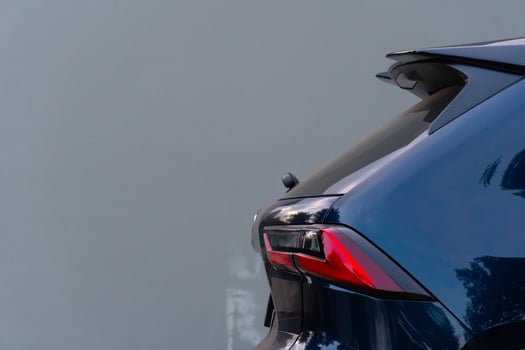 Partial rear view of a dark blue black SUV. Possibly based on the taillight design. The car is parked against a plain light-colored background. photo