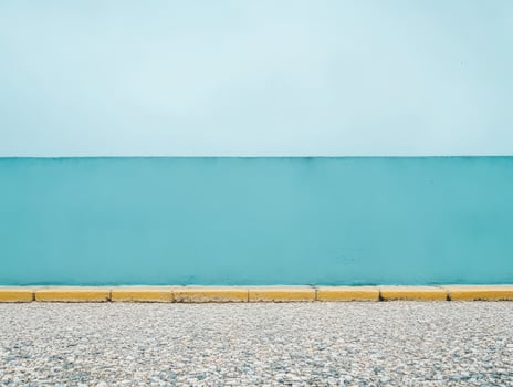 A minimalist scene featuring a blue wall against a gravel surface and a yellow curb. photo