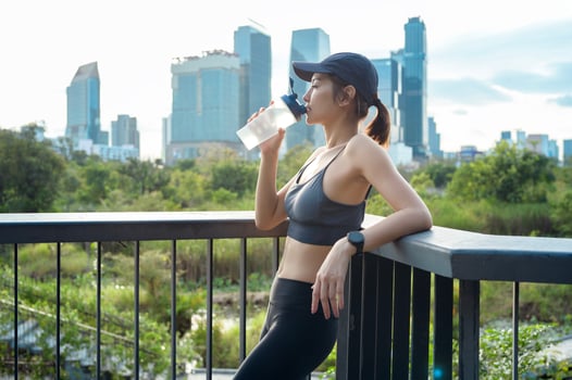 Young Woman Enjoys a Refreshing Drink While Relaxing on a Balcony Overlooking a City Skyline photo