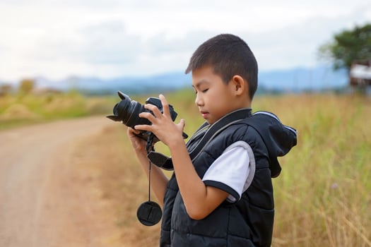Asian boy uses digital camera to take nature photos in a field. Concept of exploration, outside the classroom, outdoors, ecology, nature, learning, travel.