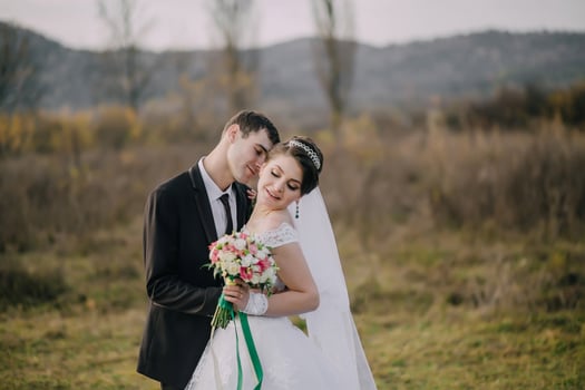 groom kisses bride in field with mountains in background photo