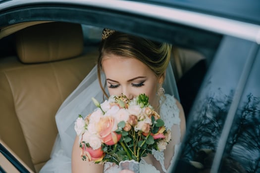 Bride sitting in car and looking at bouquet of flowers photo