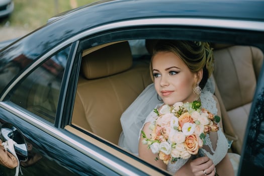 A woman in a wedding dress is sitting in a car with a bouquet of flowers. photo