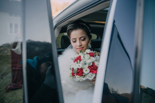 bride is getting into a car with a bouquet of flowers photo