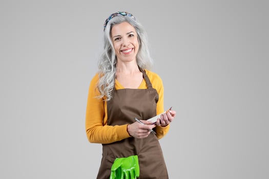 A middle aged woman dressed in a casual outfit is happily gardening, holding a pair of gardening gloves. Her gray hair is styled neatly, reflecting her passion for farming and outdoor activities. photo