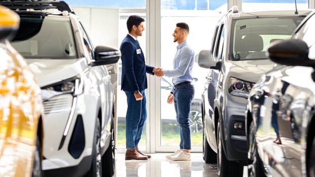 Wealthy middle-eastern man standing among luxury cars in showroom and shaking sales manager hand, celebrating successful deal. Arab guy buying brand new comfortable auto in salon, full length photo