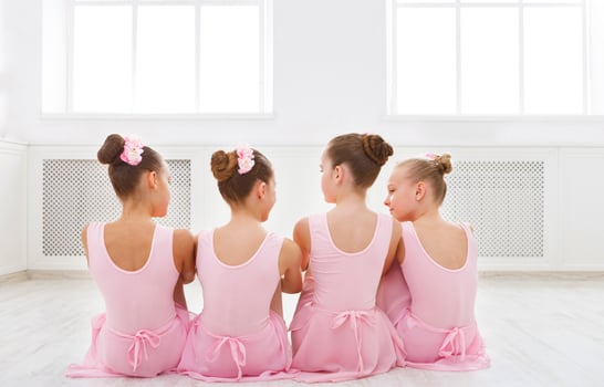 Little ballerinas talking in ballet studio. Group of girls having break in practice, sitting on floor, back view. Classical dance school photo