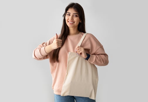 Zero Waste. Millennial Woman Showing Blank Eco Bag And Gesturing Thumbs Up Posing Standing On White Studio Background, Smiling To Camera. I Like Ecology Friendly Lifestyle, No More Plastic Concept photo