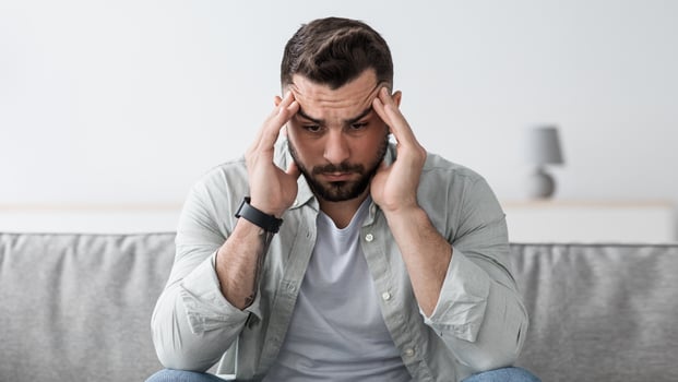 Dramatic lifestyle, migraine, middle age crisis, bad feeling, health problems. Worried person indoors. Sad attractive muscular bearded man sitting on sofa suffering from headache in room interior photo