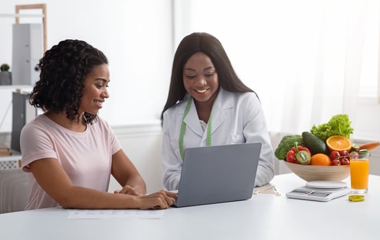 Black women nutritionist and patient looking at laptop screen at clinic, making diet plan, copy space photo