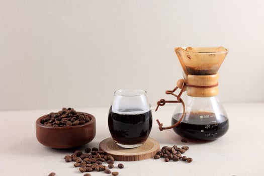 Glass Chemex Coffeemaker with Tasty Drip Coffee and Beans on Cream Table photo