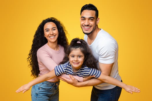 Portrait Of Happy Middle Eastern Parents Playing With Their Little Daughter, Adorable Arab Girl Having Fun With Mom And Dad, Pretending Flying, Spreading Hands, Imitating Plane Over Yellow Background photo