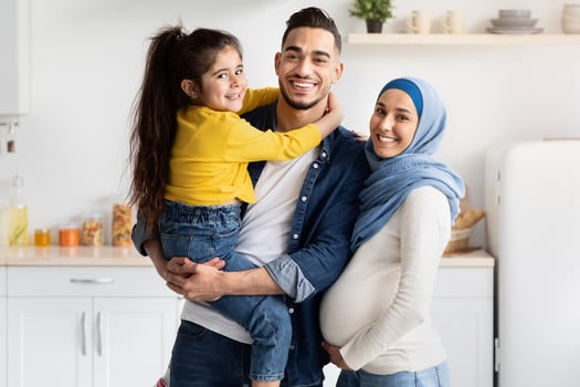 Portrait Of Smiling Muslim Family With Pregnant Mother And Little Female Kid Posing In Kitchen Interior, Happy Expecting Islamic Parents And Their Cute Daughter Embracing And Smiling At Camera photo
