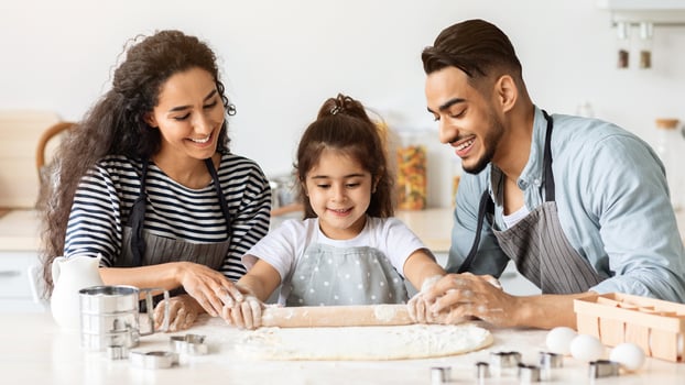 Smiling middle-eastern family parents and kid making biscuits together at home, rolling dough and having conversation, closeup. Happy arab father, mother and daughter baking at kitchen photo