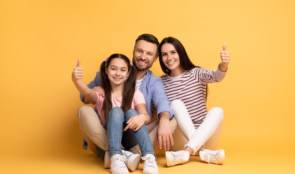 A cheerful family of three poses together with thumbs up. The father, mother, and daughter exude love and happiness in a bright yellow setting, showcasing their strong bond and joy. photo