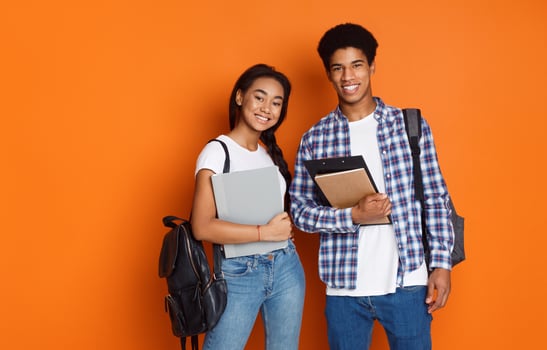 Happy students wearing backpacks and holding exercise books, orange background photo