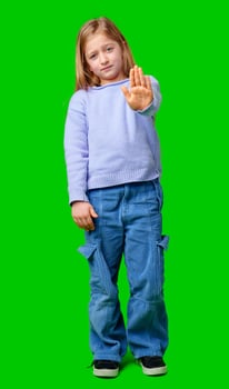 A young girl in a light purple sweater poses with her hand extended, signaling a stop gesture against green background photo