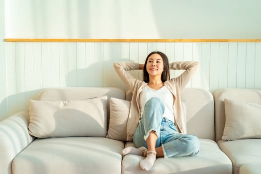 Carefree Asian woman relaxing and sitting on a sofa at home in the morning photo