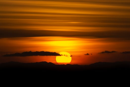 Silhouette mountain with sun and line clouds in sunset sky. photo