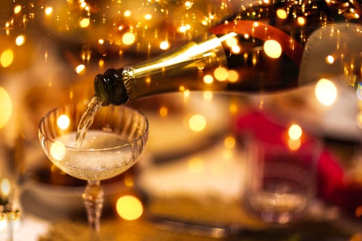 Champagne is poured from bottle into stylish glass. Sparkling golden festive lights against background. Bubbles rise in sparkling wine. photo