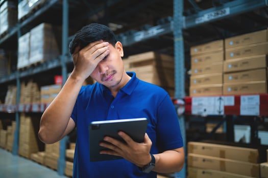 A man in a blue shirt is looking at a tablet while holding it in his hand. He is in a state of confusion or frustration photo
