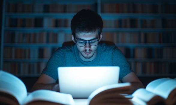 A focused individual studying on a laptop surrounded by books at night. photo