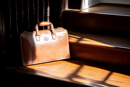 A vintage leather briefcase rests on wooden stairs, illuminated by sunlight. photo