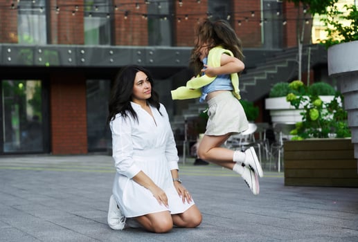 Mother and daughter playfully interacting outdoors in a modern urban setting during the day photo