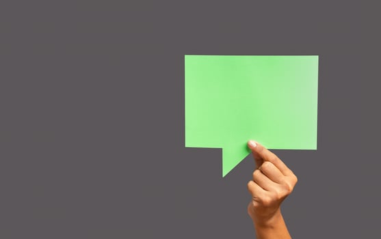 Close-up of hand holding a green speech bubble against a gray background photo