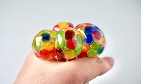 Hand squeezing colorful water beads rubber squeeze stress ball isolated on horizontal white background. photo