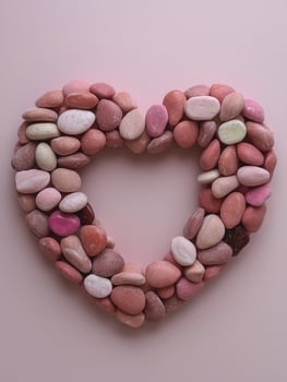 Heart shaped arrangement of pink and white candy stones on a pink background photo
